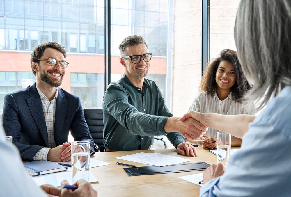 Happy Businessman And Businesswoman Shaking Hands At Group Board Meeting